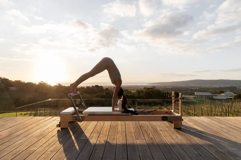Woman using a Pilates reformer outdoors at sunrise with scenic coastal views