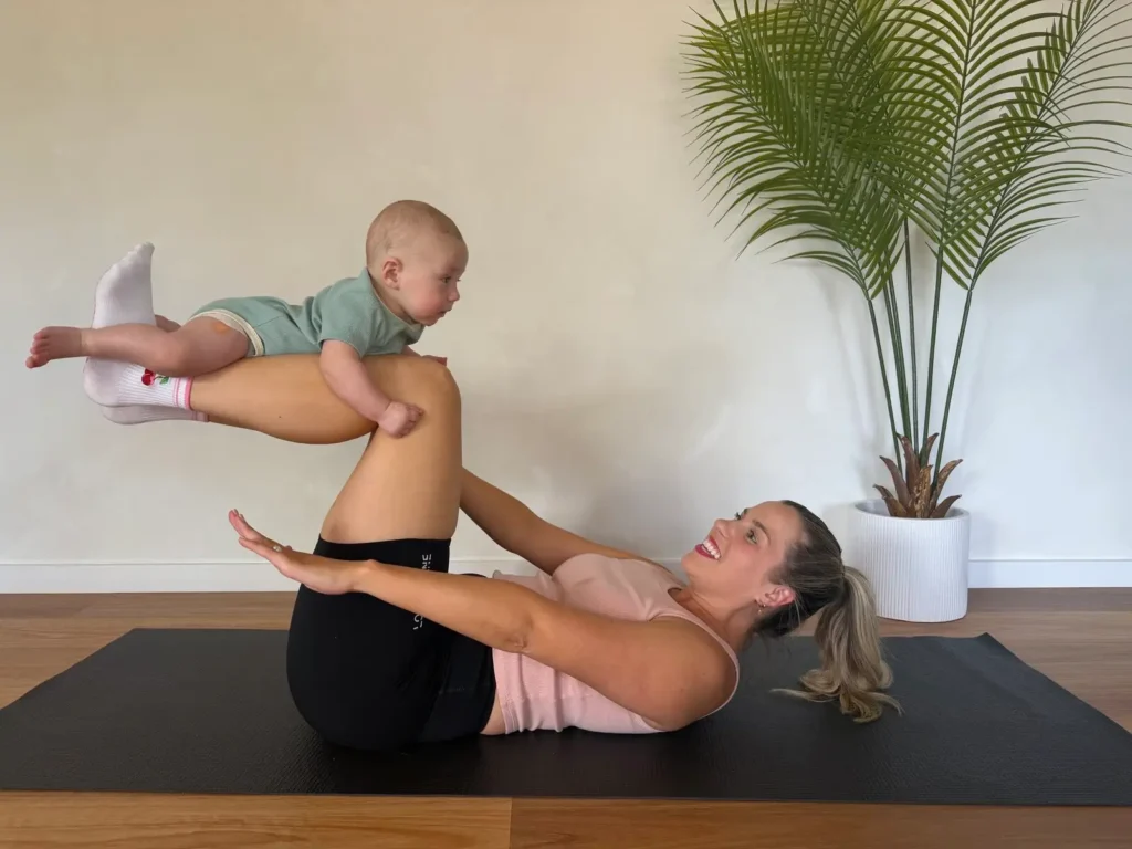 Mum and bub Pilates session with mother balancing baby on her legs on a mat
