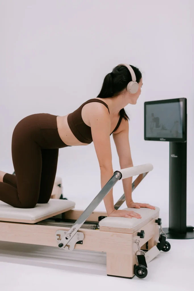 Woman using a Pilates reformer with headphones and digital screen in a minimalist studio